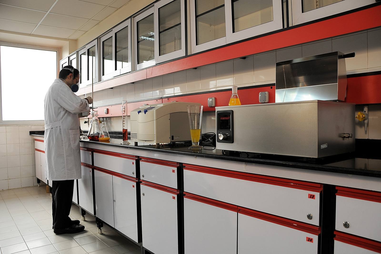 Analyst working at a Scientora-built laboratory bench run with overhead reagent shelving, epoxy worktops and a stainless fume enclosure